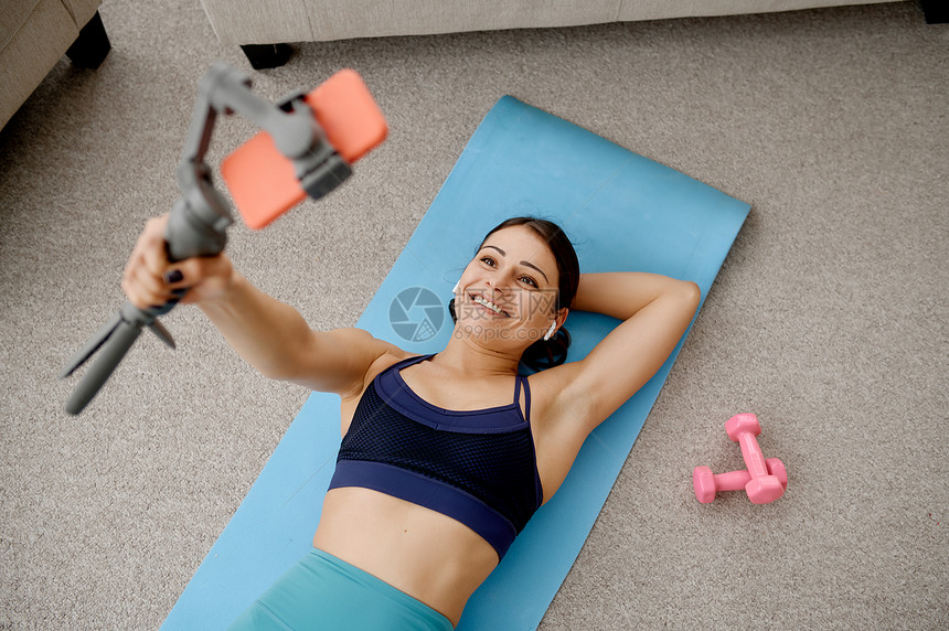 穿着运动服参加互联网体育锻炼背景室内工作坐在垫子上的妇女与电话进行在线健身培训的妇女图片