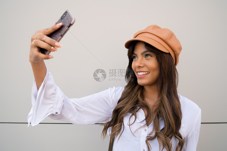 年轻女在户外站立时用摩菲手机自拍的肖像城市概念图片