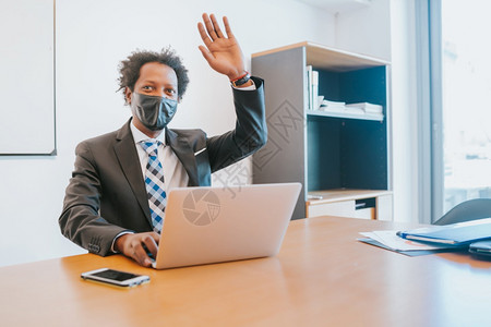 专业商人戴面罩在办公室用笔记本电脑工作时向某人打招呼图片