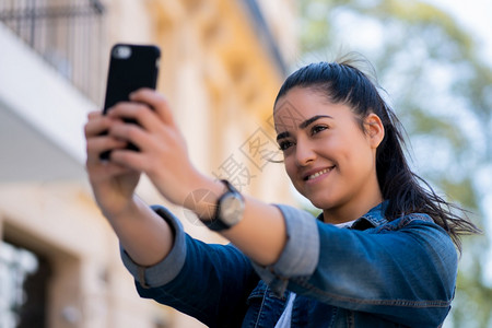 嗜酒年轻女在户外站立时用摩菲手机自拍的肖像城市概念背景
