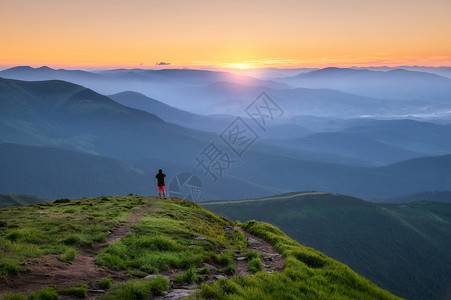 山顶上的运动男子在山峰上仰望着谷在欧洲夏季的多彩日落时阳光照耀着太有旅行者迷雾山森林陷落令人惊叹的天空和阳光风景背景图片