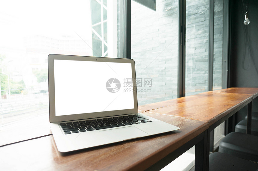 在办公室窗口技术概念前面的木制桌子上有空白屏幕的笔记本电脑图片
