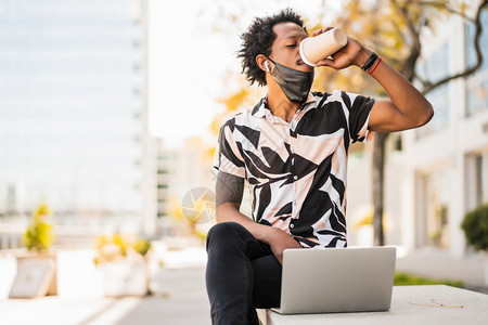 Afro旅游男子使用笔记本电脑的肖像坐在户外喝咖啡图片