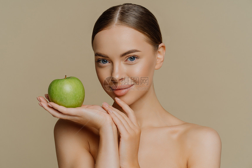照片中黑发年轻女梳着头发新鲜的绿苹果用自然化妆品肩膀与棕色背景隔绝图片