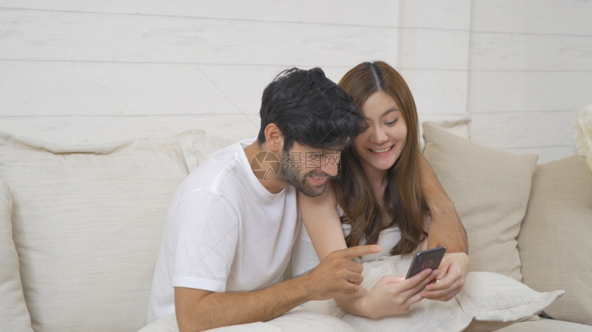 一对夫妇家庭中东青年快乐和亚洲女在社交媒体互联网上使用智能手机和在家沙发上坐着的人技术设备中的生活方式多种族裔图片