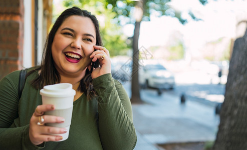 年轻又大的女人肖像在街上用电话交谈同时在户外喝咖啡城市概念图片