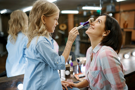 妈和小女孩一起玩发型师快乐的童年迷人家庭女儿在沙龙给妈化妆图片