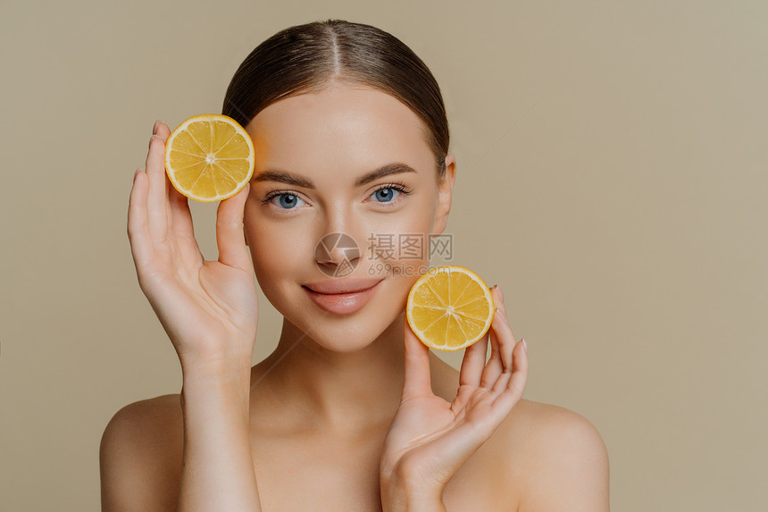 有深色梳发的棕年轻女人肖像直视照相机紧握着两片柠檬无顶架皮肤健康发光隔绝在米底图片