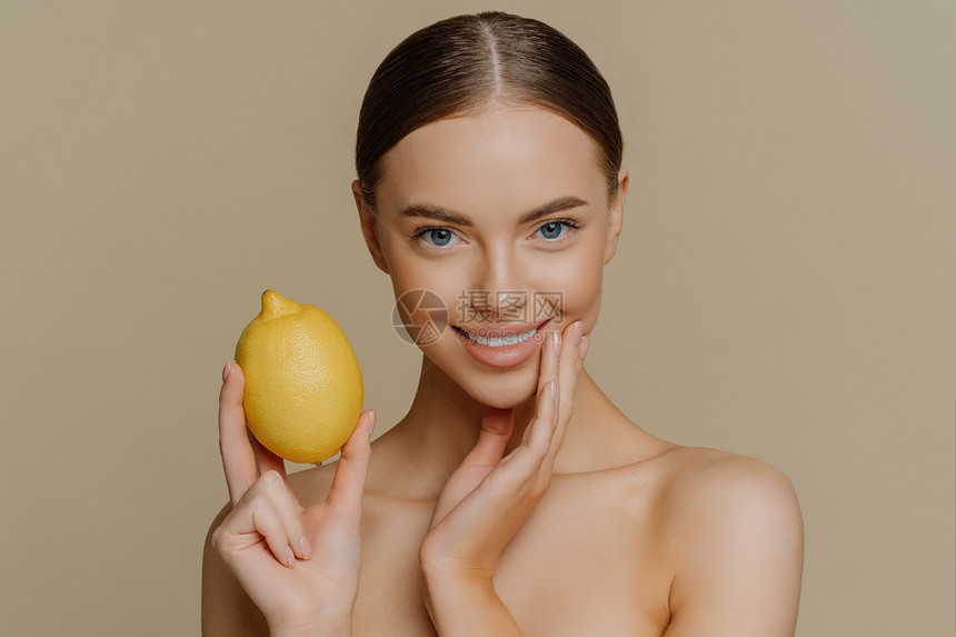 欧洲健康女横向镜头使用柠檬做天然面罩照顾她的身体皮肤无上室内隔离在棕色背景之上图片