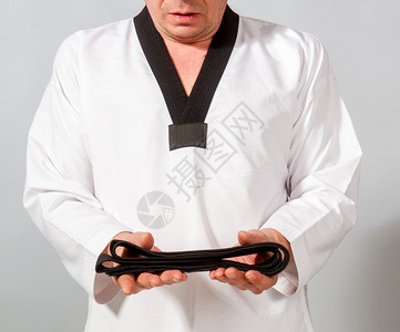 跆拳道黑带白色铁拳道和服的强壮男运动员得到了当之无愧的黑带背景