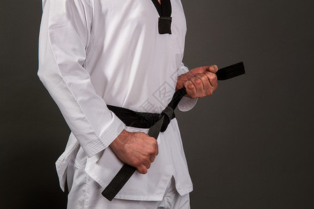 白色台拳道和服的强壮男运动员将黑带系在感知的上图片