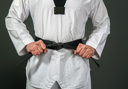 白色台拳道和服的强壮男运动员将黑带系在感知的上背景图片