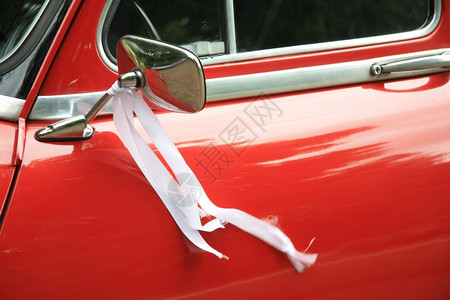 一辆古老的红色车镜子上有白色丝带作为结婚装饰图片