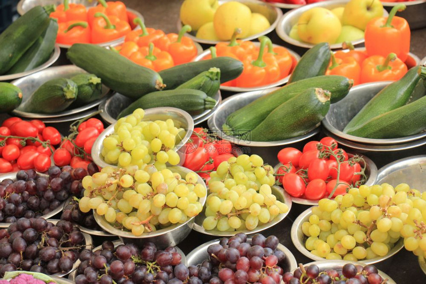 市场摊位上新鲜水果和蔬菜小金属碗中展示的葡萄西红柿椰菜和胡椒图片