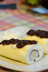 装满白奶油和香蕉的饼干卷装满巧克力糖浆装在白盘上图片