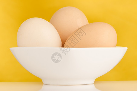 黄色背景碗里三个黄色的鸡蛋图片