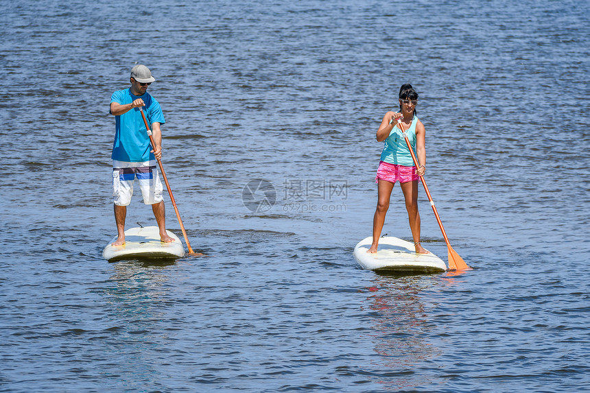 男女在湖上站起滑板年轻夫妇在湖上渡水男女游客在暑假期间穿游泳衣图片