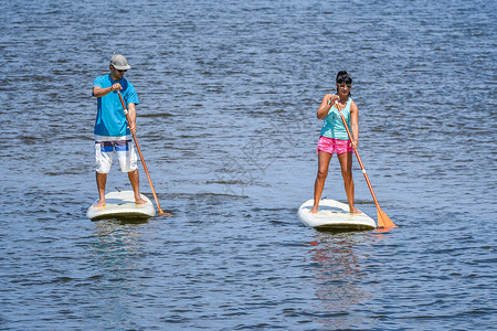 男女在湖上站起滑板年轻夫妇在湖上渡水男女游客在暑假期间穿游泳衣图片