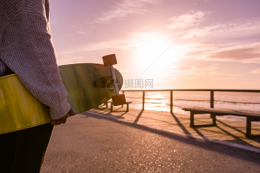 女孩在日落时海滩附近拿着滑板图片