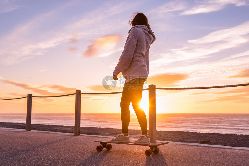 女孩在日落时海滩附近的滑板上骑着图片