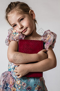 金发可爱的小女孩拥抱着一本红书在白色背景面前图片