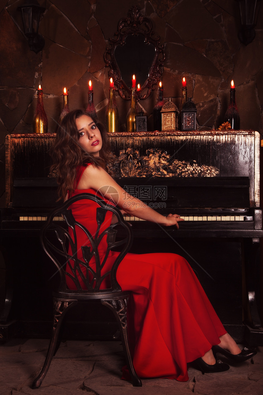在钢琴附近穿红裙子的美丽黑发女图片