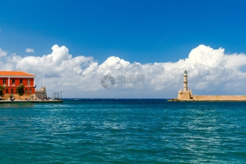 在古老的Chania港的灯塔蓝海和云彩的背景之下图片