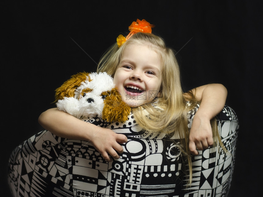 一个小女孩在椅子上有一个柔软的玩具椅子被布置了女孩靠在椅子上手被挂在椅子上手被挂在肩膀上小玩具黑色背景图片