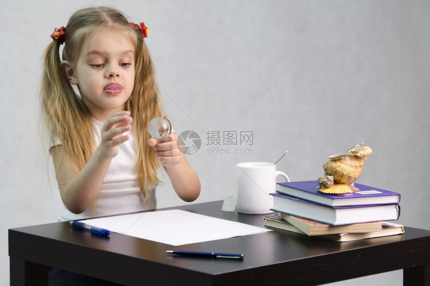 女孩若有所思毫不费力地转动一个小玻璃球坐在桌边墓中有书籍纸张钢笔玻璃球一杯茶贝壳作者的形象图片