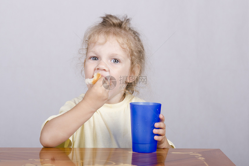 坐在桌边的两岁女孩吃松饼喝塑料杯酒图片