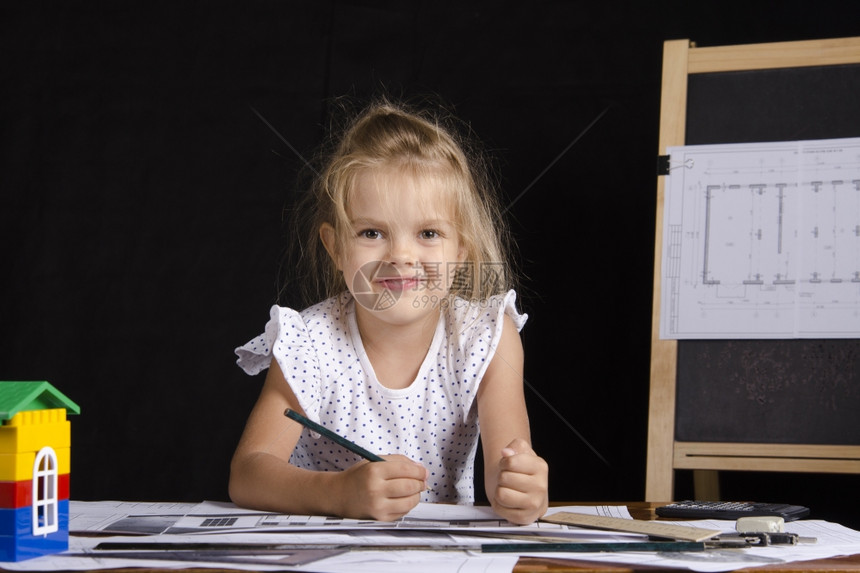 4岁女孩在建筑师的画像中坐在桌子上的女孩与图画一起坐在桌子上背景中是董事会的画作图片