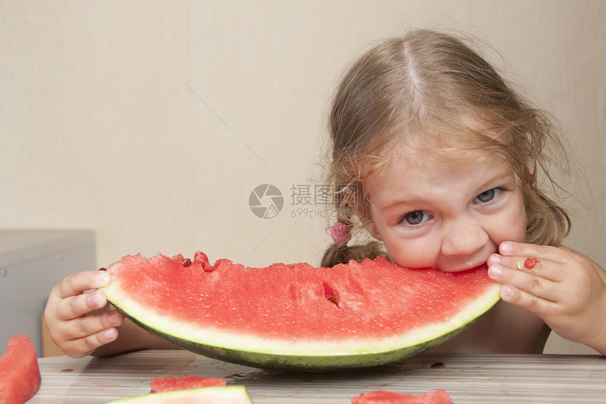 两岁的女孩坐在厨房桌边吃着快乐的西瓜图片