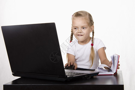 女孩坐在桌子上是笔记本电脑女孩工作愉快地看另一只笔记本电脑打开笔记本电脑背景图片