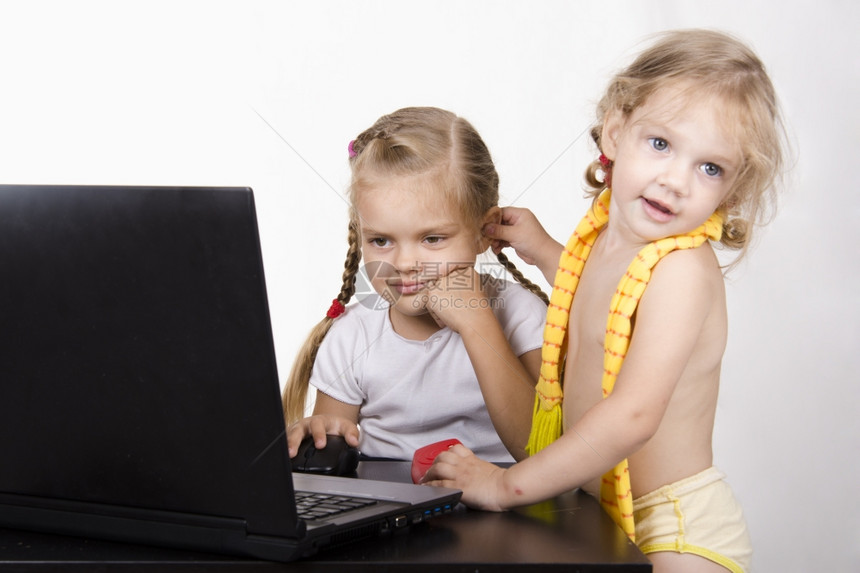 坐在桌子上的女孩在桌子上是一台笔记本电脑它起作用的女孩图片