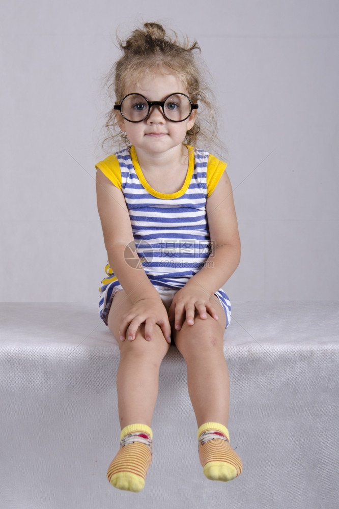 工作室两岁的女孩坐在桌子上被白布覆盖着看照片女孩穿有趣的眼镜双手躺在我的膝上图片