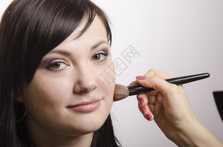 化妆过程中的师时的品粉放在一个漂亮女孩的脸上背景图片