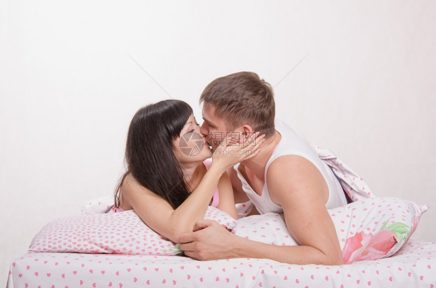 年轻美丽的女孩和男人亲吻抱在床上图片