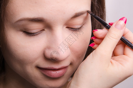 化妆师在品中画着美丽的年轻女孩眉毛背景图片