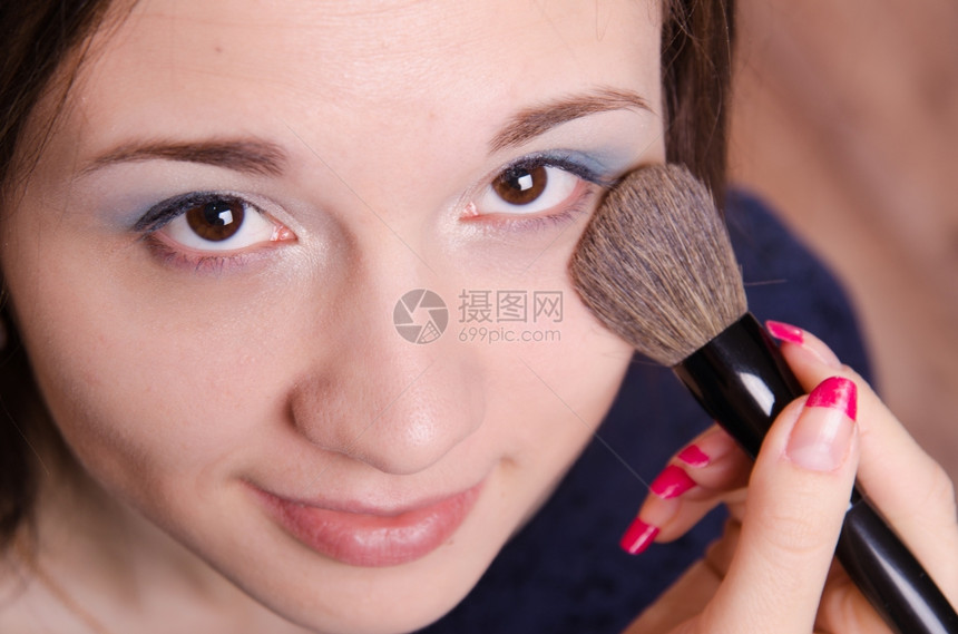 化妆师在时将粉涂在美丽的年轻女孩脸上图片