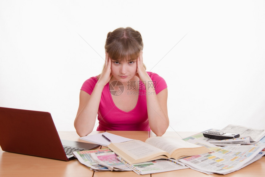 一名年轻女孩坐在一张桌子上坐在一张桌子上有堆报纸百科全书和一台笔记本电脑图片