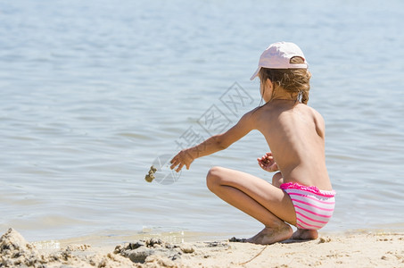 女孩坐在河岸上扔沙子在水里图片