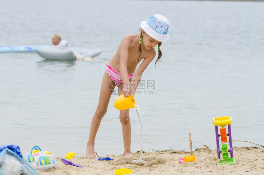 5岁女孩在海滩上从沙中的桶里倒水有趣的5岁女孩在海滩上玩沙模图片