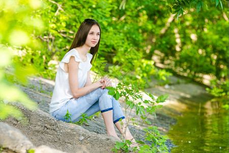 一位女孩坐在河的水泥岸上可爱的欧裔女孩坐在河的水泥岸上图片