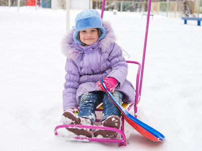 雪天里坐在雪橇上的快乐女孩坐在雪橇上的蓬乱而快乐的五岁女孩图片