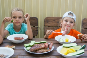 两个小女孩坐在木桌上吃烤香肠图片