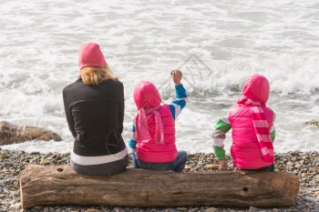 两个女孩和人坐在沙滩上的原木向水里扔石头图片