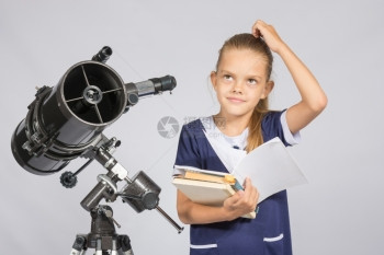 女学生在望着远镜时一边站在望远镜旁一边看教科书图片