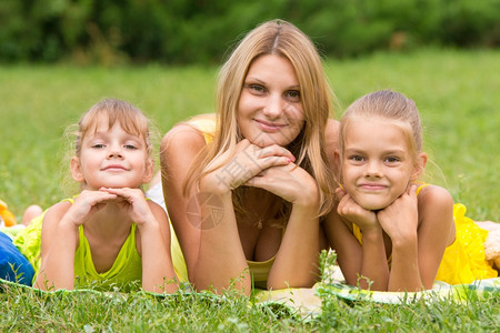 母亲和两个女儿躺在绿草上举起双手头抬一只看着照片图片