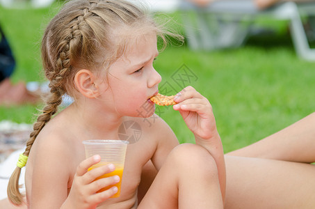 女孩吃饼干喝一个塑料可支配杯子里的果汁图片