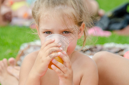 女孩在野餐时喝一个塑料可支配杯子里的果汁图片